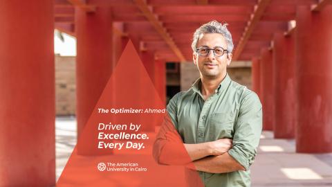 A male wearing glasses is standing next to red pillars. Text reads "The Facilitator: Ahmed. Driven by Excellence. Every Day. ϲͼ"