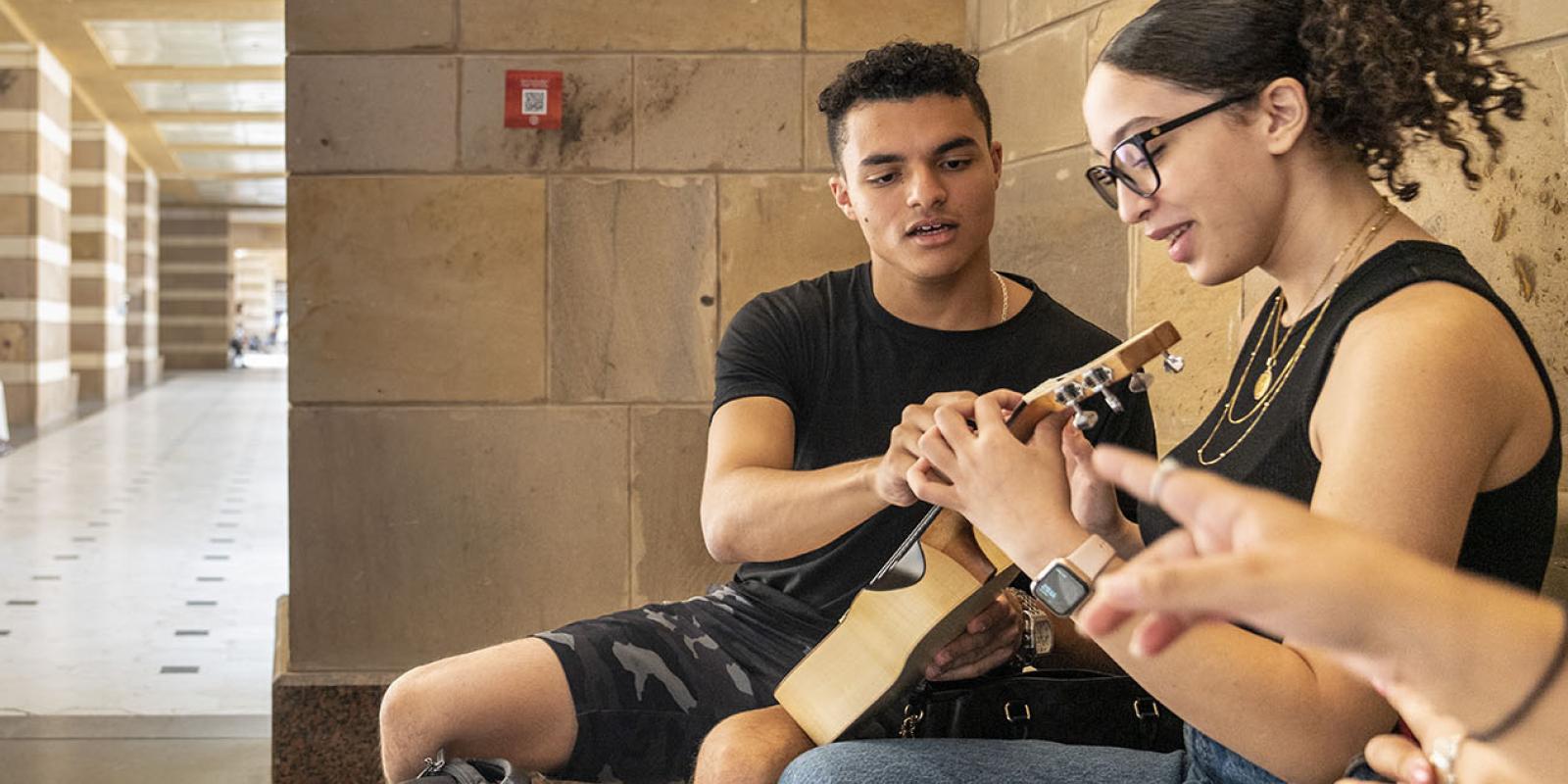 A girl and boy on ϲͼ campus playing the guitar