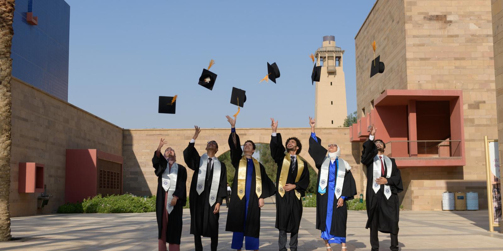 A group of students wearing gowns and throwing their cap in the air on ϲͼ campus