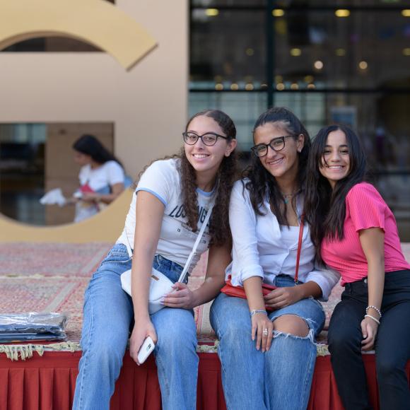 three smiling girls sitting on a stage in ϲͼ plaza